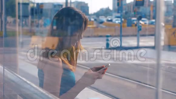 坐在公共汽车或地铁车站的年轻迷人的女人两次曝光女孩用她的手机输入信息视频的预览图