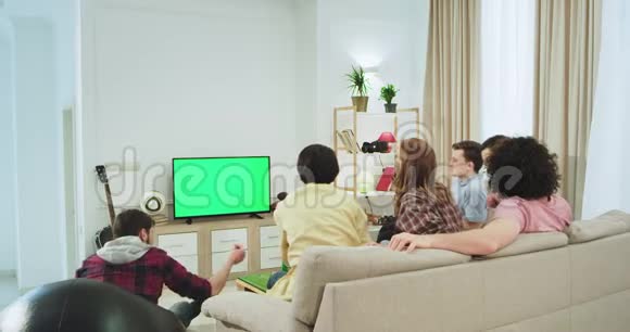 电视上的绿色屏幕一大群朋友在沙发上在一个宽敞的客厅里看电视上的东西多种多样视频的预览图