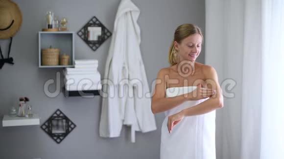 淋浴后裹着毛巾的漂亮女人在她的胳膊肘上涂了奶油视频的预览图