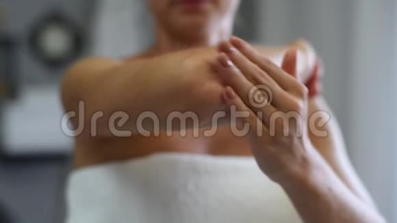 淋浴后裹着毛巾的漂亮女人在她的胳膊肘上涂了奶油视频的预览图