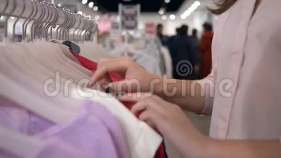 在销售折扣期间女性在商店的衣架上挑选新的时尚服装手握不集中的背景视频的预览图