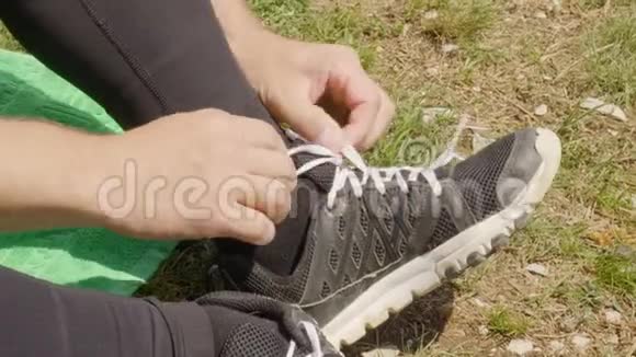 男性在户外休息时双手解开运动鞋上的鞋带穿着运动鞋坐在草地上的人的鞋带视频的预览图