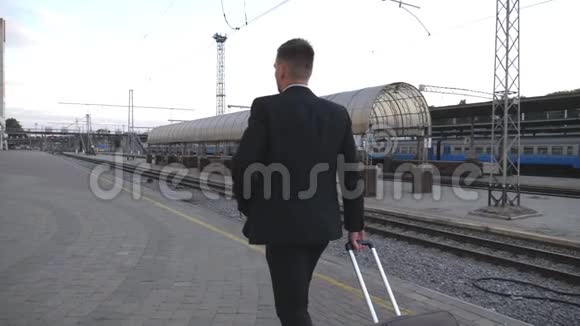 不可辨认的成功商人西装革履地穿过火车站把手提箱拉到车轮上照相机视频的预览图