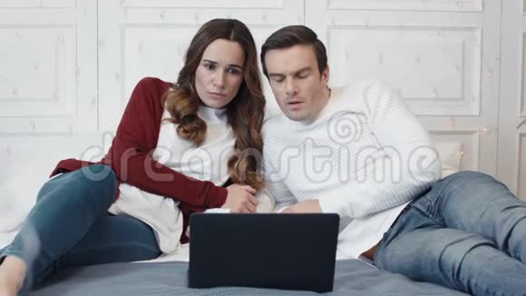 悲伤的一对夫妇在家里一起在电脑上看可怕的消息视频的预览图