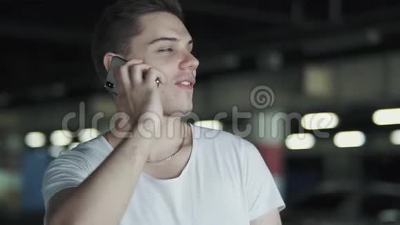 穿着白色t恤的快乐男站在地下停车场用手机说话视频的预览图
