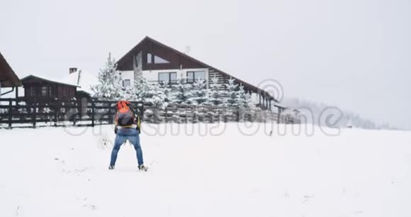 在寒冷的冬天一个滑雪游客和一只白山狗玩耍在他山顶上的BNB房子旁边视频的预览图