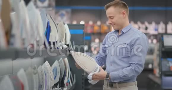 一个穿衬衫的年轻英俊的男人在一家消费电子商店里选择熨斗学士视频的预览图