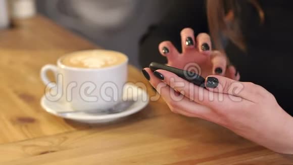 一个年轻女孩在咖啡馆里的特写镜头手里拿着拿铁和电话视频的预览图