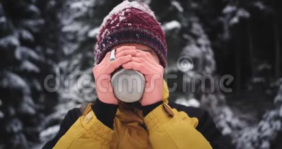 一位年轻的游客带着一张漂亮的脸在山上喝着铁杯里的茶他已经冻僵了视频的预览图