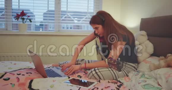 在卧室里一个十几岁的女孩在她的笔记本上打字非常集中然后在她之后打开她的平板电脑视频的预览图
