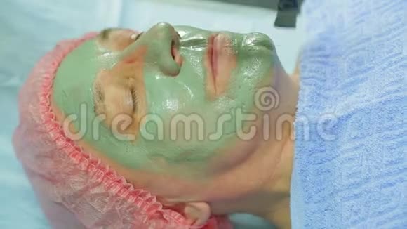 一位女性美容师用刷子把一个治愈泥面具涂在男人的脸上侧视视频的预览图