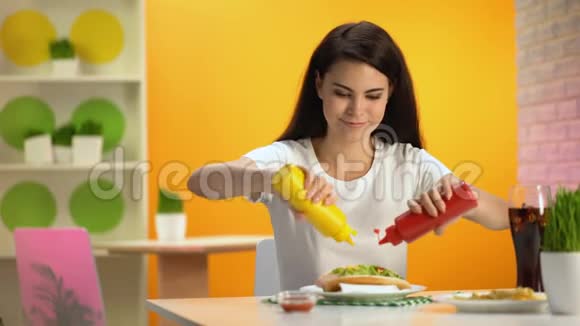 年轻女士在热狗上浇番茄酱和芥末并在相机上微笑食堂视频的预览图