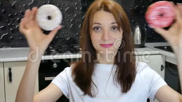 在厨房里一位留着长发的滑稽女孩用红白甜甜圈在她的眼睛上玩得开心视频的预览图