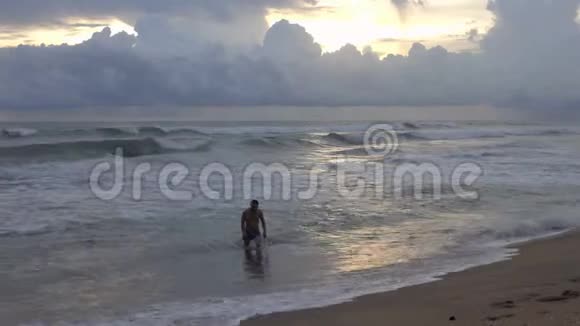 日落时分年轻人从海滩上的热带海洋中走出来视频的预览图