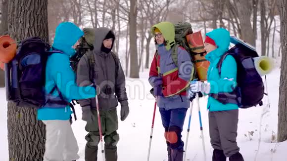 年轻的游客穿着暖和的夹克拿着背包在冬天的森林里聊天和讨论视频的预览图