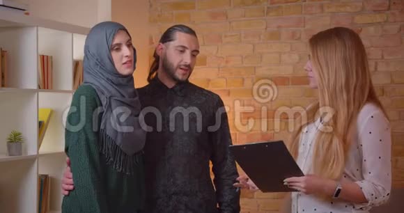 一对年轻快乐的穆斯林夫妇和一个真正的人讨论一个新公寓兴高采烈地拥抱在室内视频的预览图