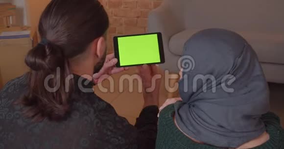 用带有绿色屏幕的平板电脑拍摄年轻快乐的穆斯林夫妇的特写后景视频的预览图