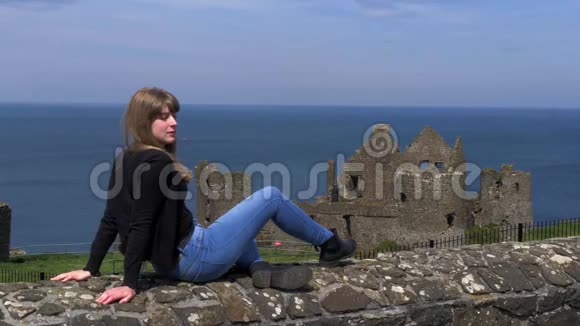 女孩在北爱尔兰的Dunluce城堡的墙上放松视频的预览图
