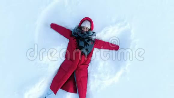 穿着红色羽绒服的女孩做了个雪天使空中摄影机以螺旋上升俯视视频的预览图