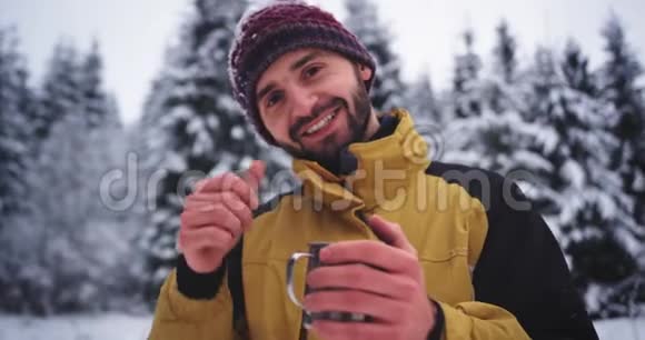 微笑的游客看着镜头的肖像在雪林中他拿着一个铁杯热乎乎的视频的预览图