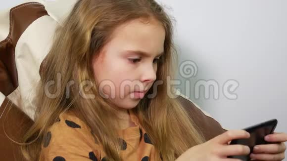 八岁的女孩带着智能手机坐在无框椅子上视频的预览图