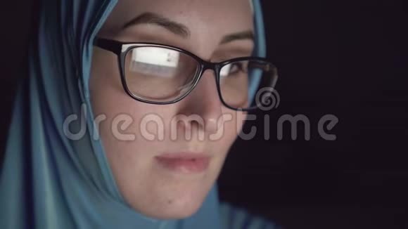 穆斯林妇女戴着头巾晚上戴着眼镜在黑暗中集中着脸上网视频的预览图