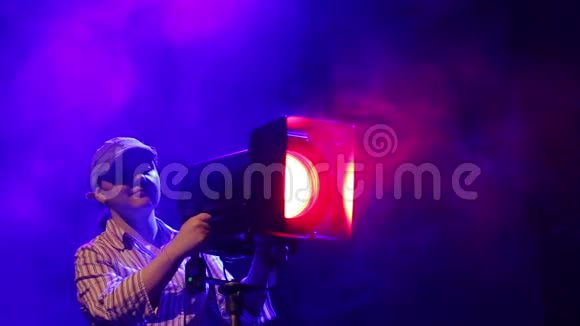 舞台上一位年轻的女照明者在烟云中用一台戏剧化的投影仪工作视频的预览图