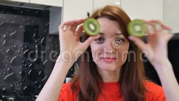 可爱的年轻妻子在厨房准备食物时玩着两半猕猴桃积极的人类情感概念视频的预览图
