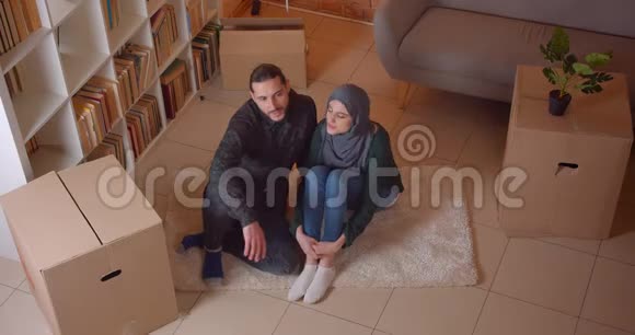 一对年轻的穆斯林夫妇坐在一间新买的公寓的地板上微笑着幸福地做梦视频的预览图
