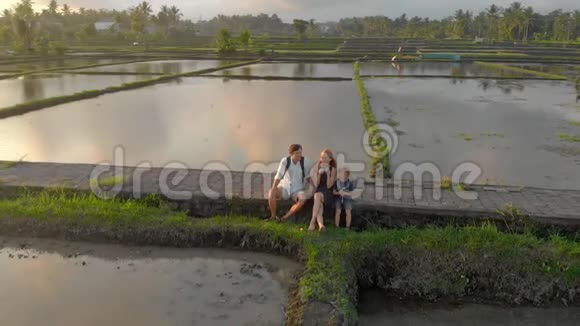一个幸福的家庭坐在人行道上穿过被水填满的大田野他们享受日落时光视频的预览图