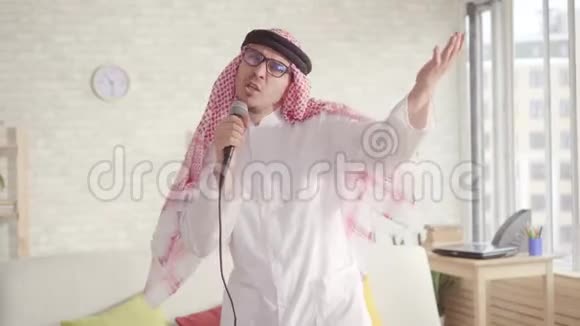穿着传统服装在家里用卡拉OK麦克风唱歌的开朗的阿拉伯男人视频的预览图