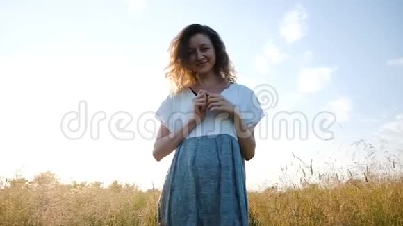 一个女人穿着一件衣服手里拿着一棵草在日落时分在田野里散步动作缓慢镜头移动视频的预览图