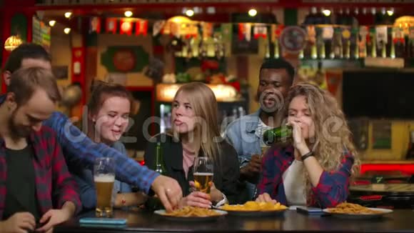 酒吧里的一大群朋友坐在桌边笑着喝着啤酒视频的预览图