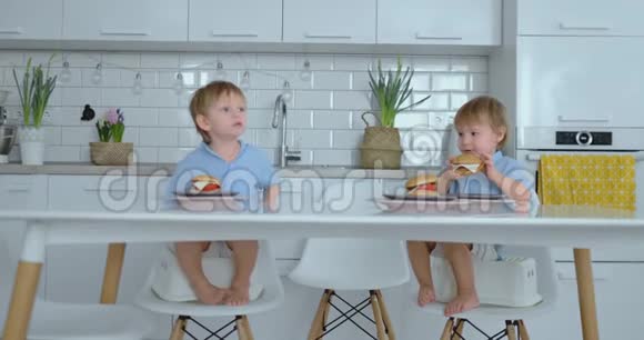 两个穿蓝色衬衫的孩子在明亮的厨房里吃汉堡视频的预览图
