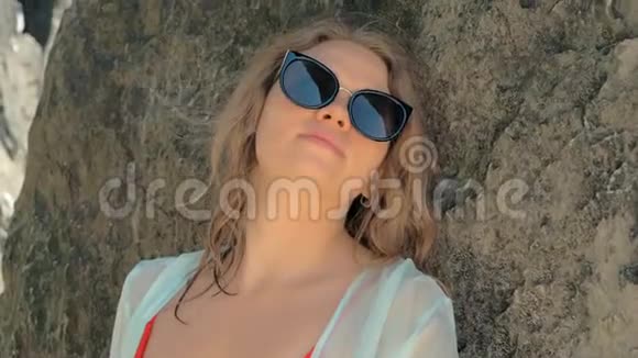 夏天戴着太阳镜的快乐女人靠在山上休息放松的女孩靠在大石头上视频的预览图