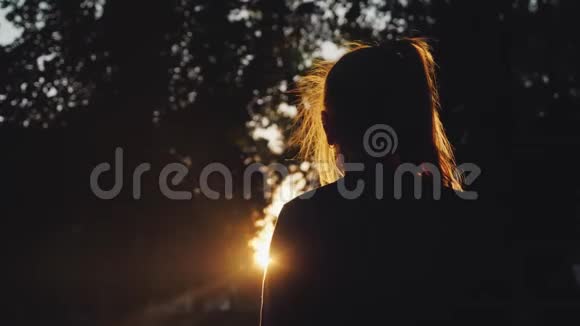 后景公园里一个女孩看日落的剪影阳光美丽地照亮了她的金发视频的预览图