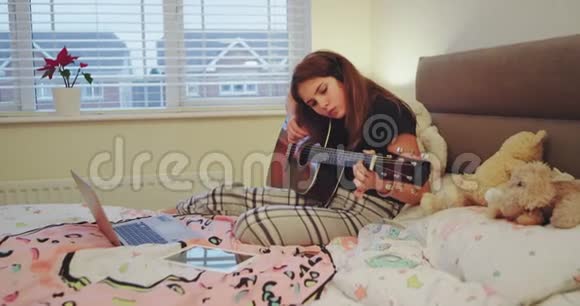 在一个舒适的卧室里年轻的女士集中弹吉他同时用笔记本视频的预览图