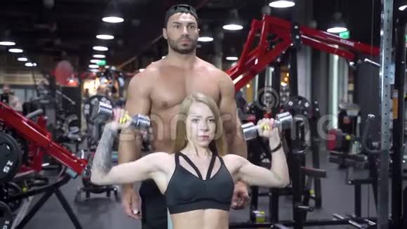 健身妇女和年轻教练男子正在健身房用哑铃锻炼肌肉视频的预览图