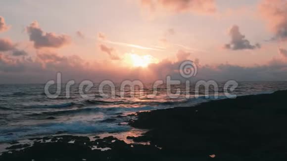 夕阳躲在云层后面美丽的粉红色日落在海上岩石海岸美丽的日落洛奇海滩浪漫之夜视频的预览图