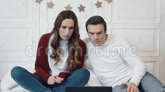 一对夫妇在家里一起在电脑上看可怕的新闻视频的预览图