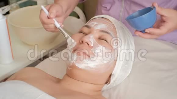 美容师在一位亚洲中年妇女的脸上涂上按摩霜美容院的振兴程序怀特公司视频的预览图