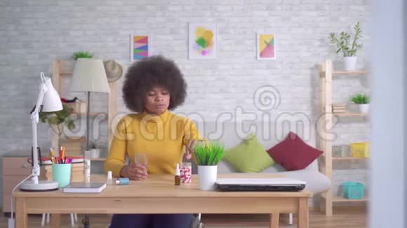 美丽的非洲裔美国妇女有非洲发型吃一片药丸喝一杯水视频的预览图