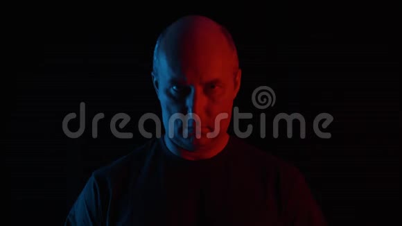 在蓝色和红色灯光下黑色背景上的成年男子肖像男人的脸在黑暗的工作室背景上寻找相机视频的预览图