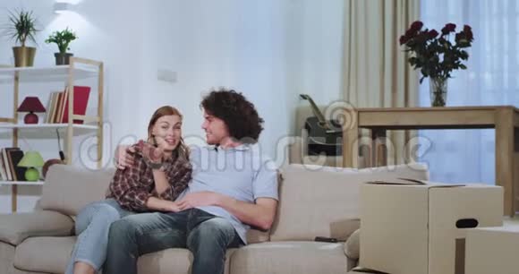 一对非常漂亮的夫妇在他们的新房子里的沙发上看电视经过了一天的艰苦活动他们享受着微笑的时光视频的预览图