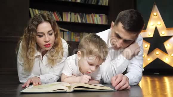年轻的家庭母亲儿子和爸爸的肖像正在一起读一本书视频的预览图