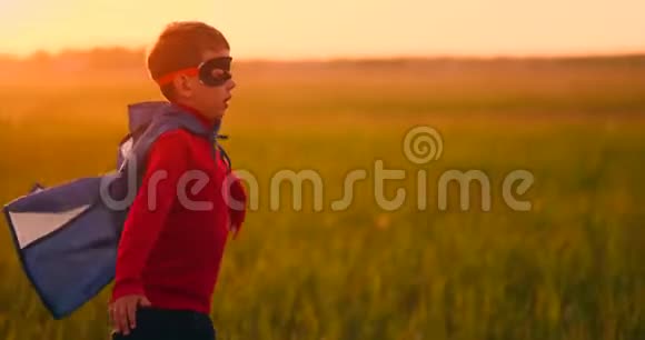 日落时分一个穿着超级英雄服装的男孩笑着跑过田野视频的预览图