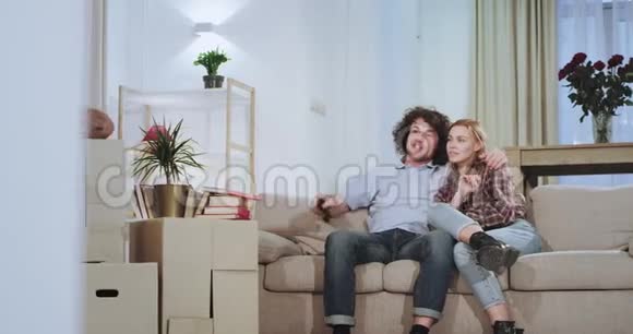 在沙发上的电视前有魅力的夫妇享受着在新房子公寓里的时光他们高兴地站起来视频的预览图