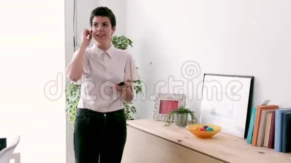 微笑的年轻商务女性用她的自由手打电话时手机站在办公室视频的预览图