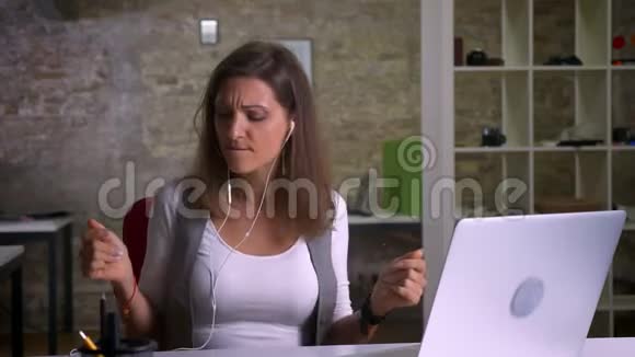 漂亮可爱的女办公室工作人员坐在笔记本电脑前一边听音乐一边跳舞视频的预览图