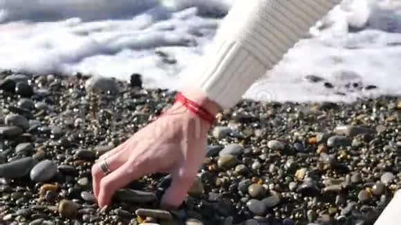 用戒指和镯子紧紧地握住男性的手触摸石头鹅卵石沙滩海浪视频的预览图